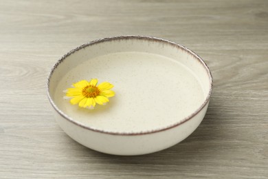Beige bowl with water and yellow flower on wooden table, closeup