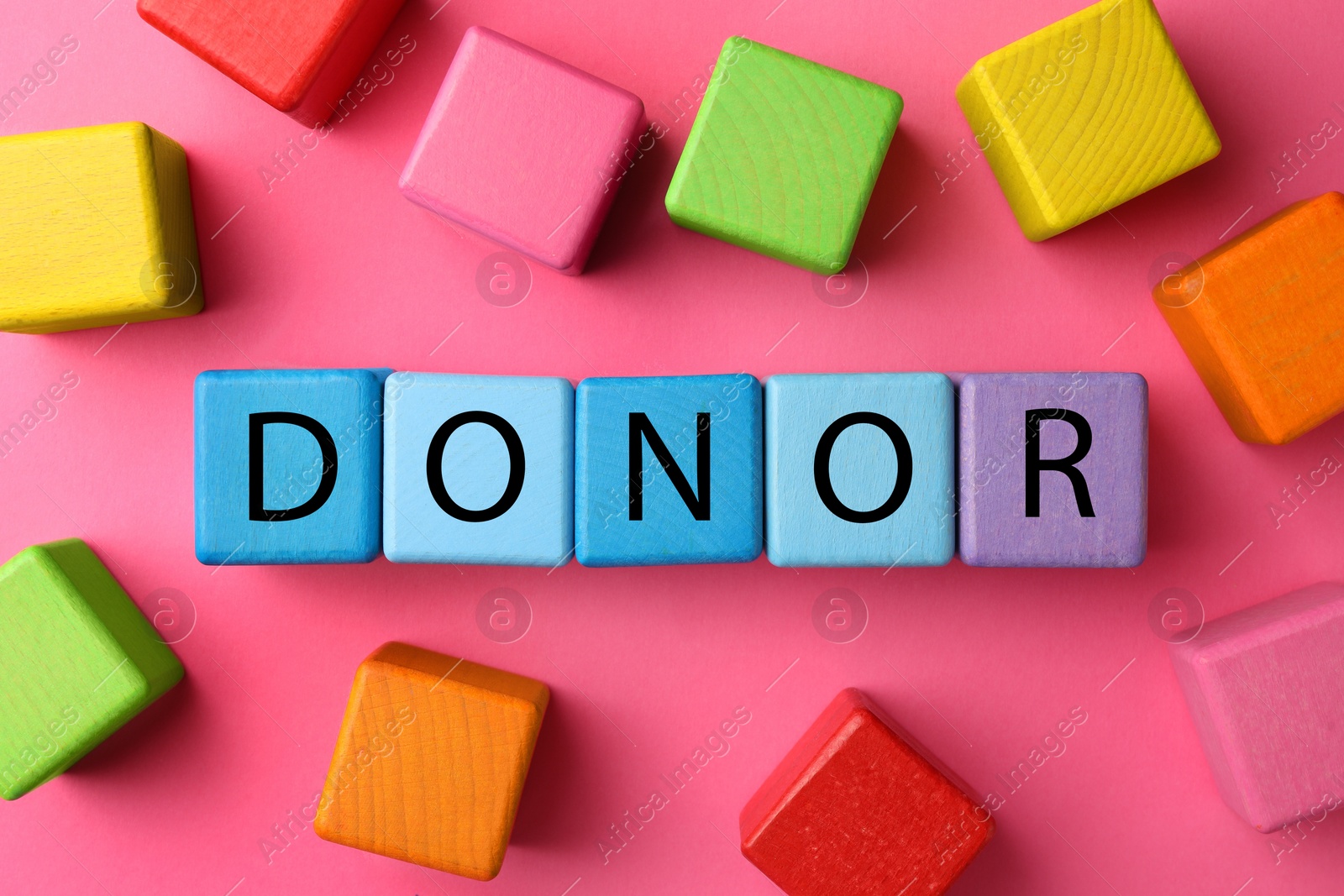 Photo of Word Donor made of colorful wooden cubes on pink background, flat lay