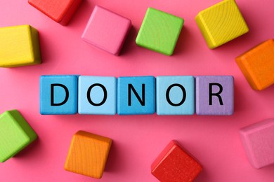 Photo of Word Donor made of colorful wooden cubes on pink background, flat lay