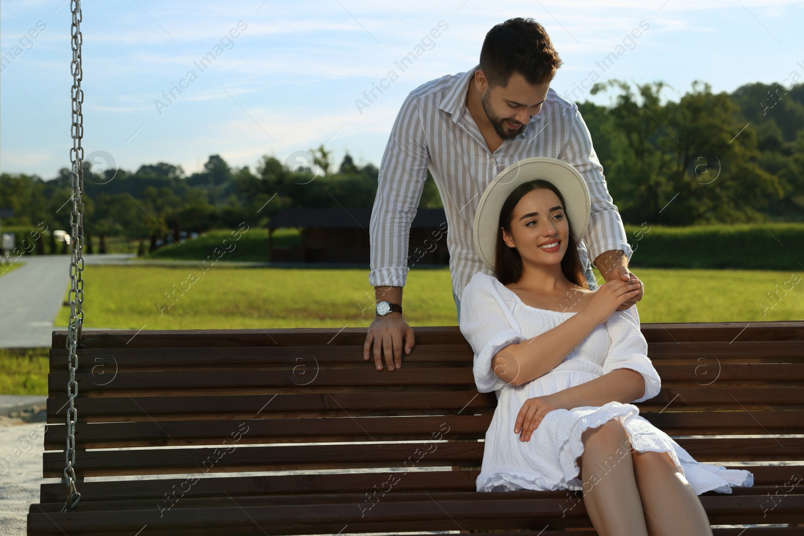 Photo of Romantic date. Beautiful couple spending time together on swing bench outdoors