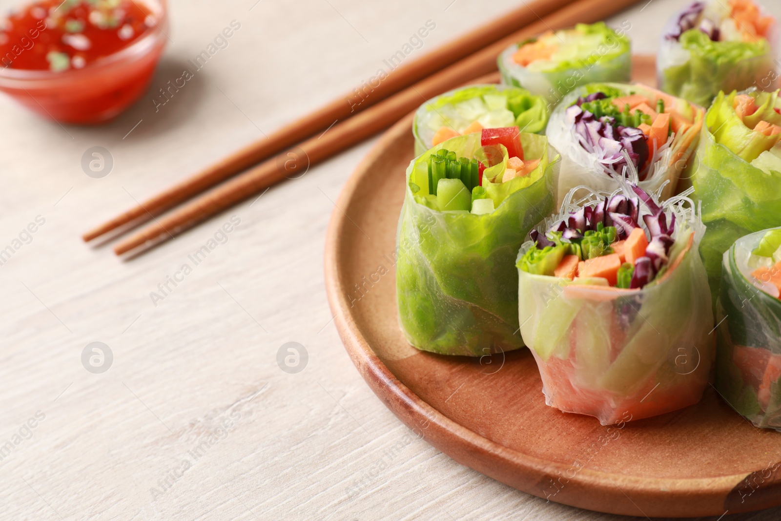 Photo of Plate with different delicious spring rolls wrapped in rice paper and chopsticks on white wooden table, closeup. Space for text