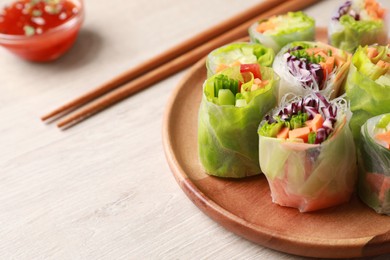 Plate with different delicious spring rolls wrapped in rice paper and chopsticks on white wooden table, closeup. Space for text