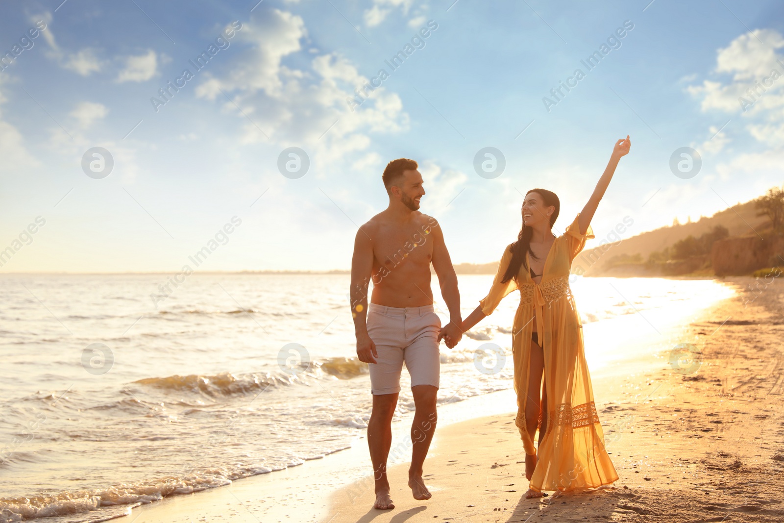 Photo of Happy young couple walking together on beach at sunset