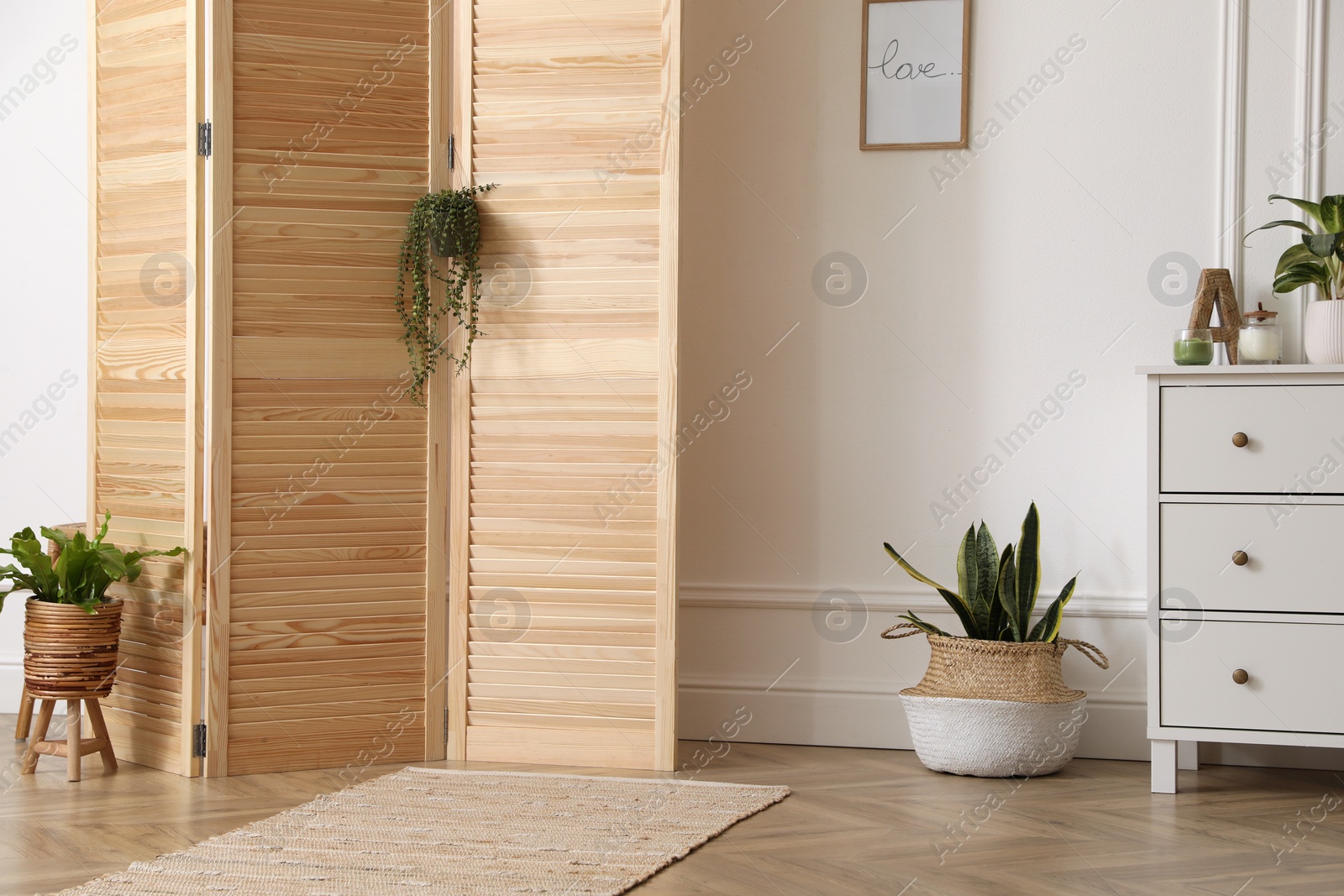 Photo of Stylish room with wooden folding screen and chest of drawers near white wall. Interior design