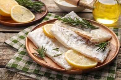 Fresh raw cod fillets with rosemary and lemon on wooden table, closeup