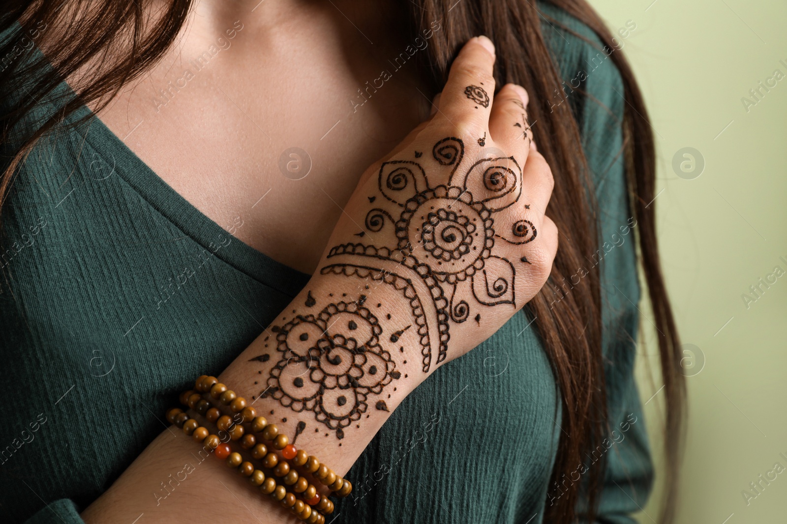 Photo of Woman with beautiful henna tattoo on hand against green background, closeup. Traditional mehndi