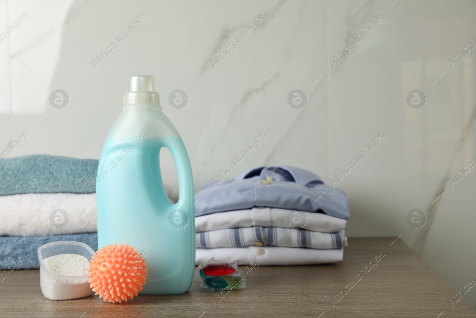 Photo of Orange dryer ball, detergents, clean towels and clothes on wooden table. Space for text