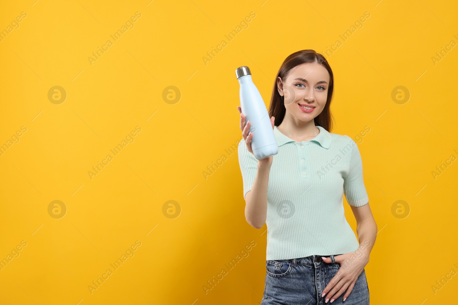 Photo of Beautiful young woman with thermos bottle on orange background, space for text