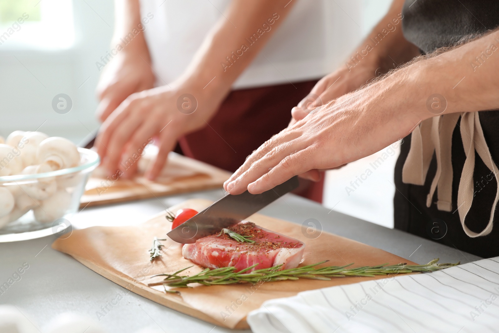Photo of Male chef cutting meat on wooden board at table, closeup