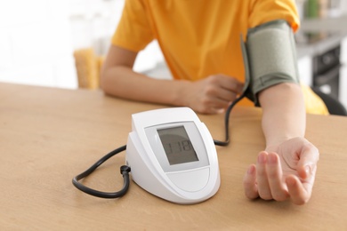 Photo of Woman checking blood pressure with sphygmomanometer at table indoors, closeup. Cardiology concept