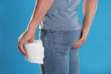 Photo of Man with toilet paper suffering from hemorrhoid on light blue background, closeup