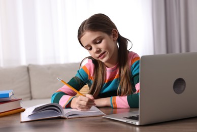 Photo of E-learning. Cute girl taking notes during online lesson at table indoors