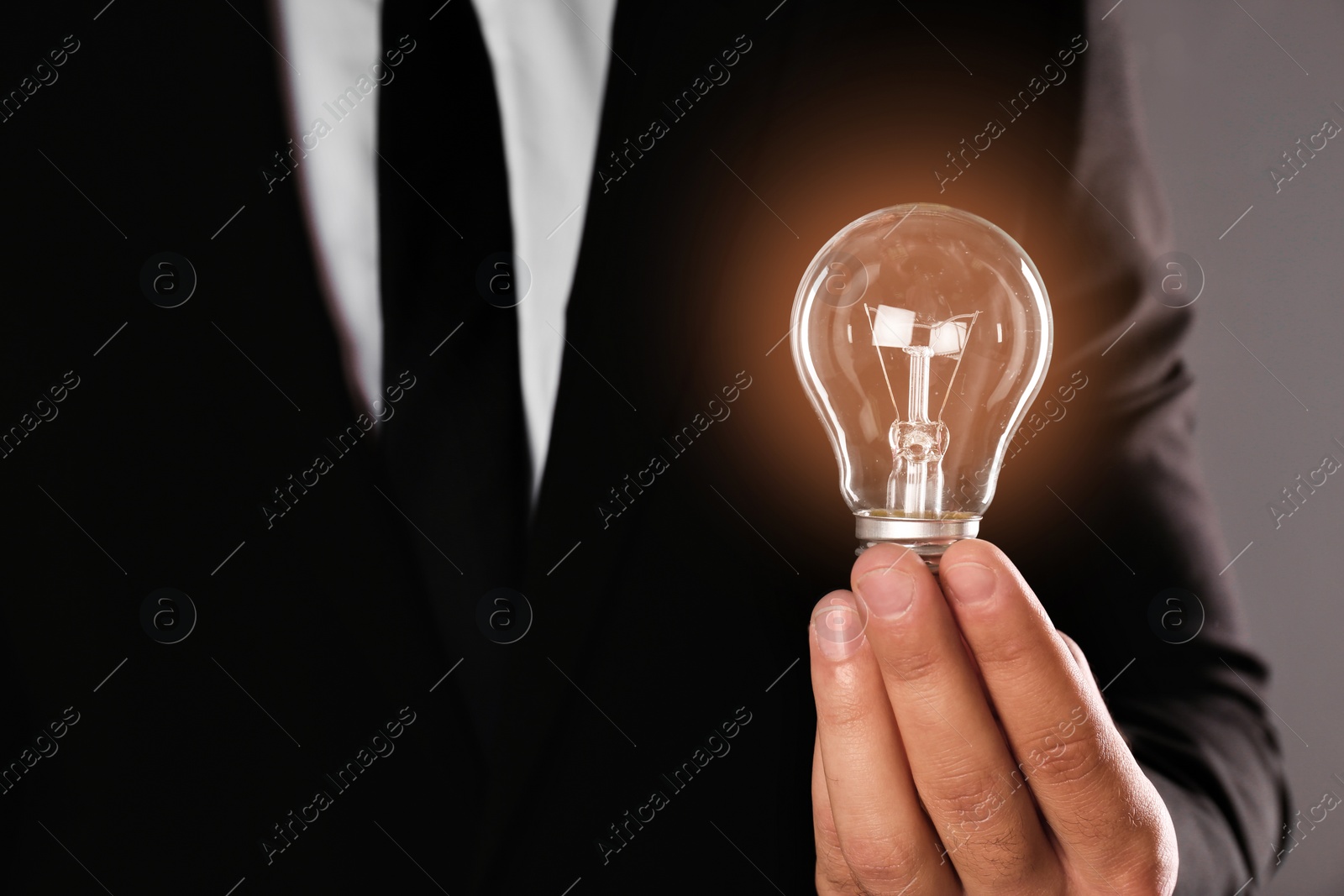 Photo of Businessman holding lamp bulb against gray background, closeup