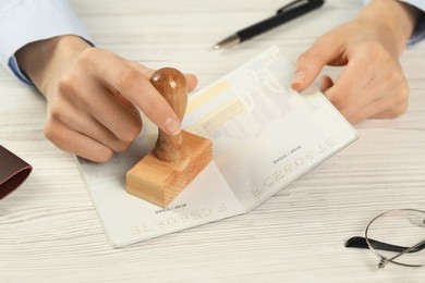 Moldova, Ceadir-Lunga - June 13, 2022: Woman stamping visa page in passport at white wooden table, closeup