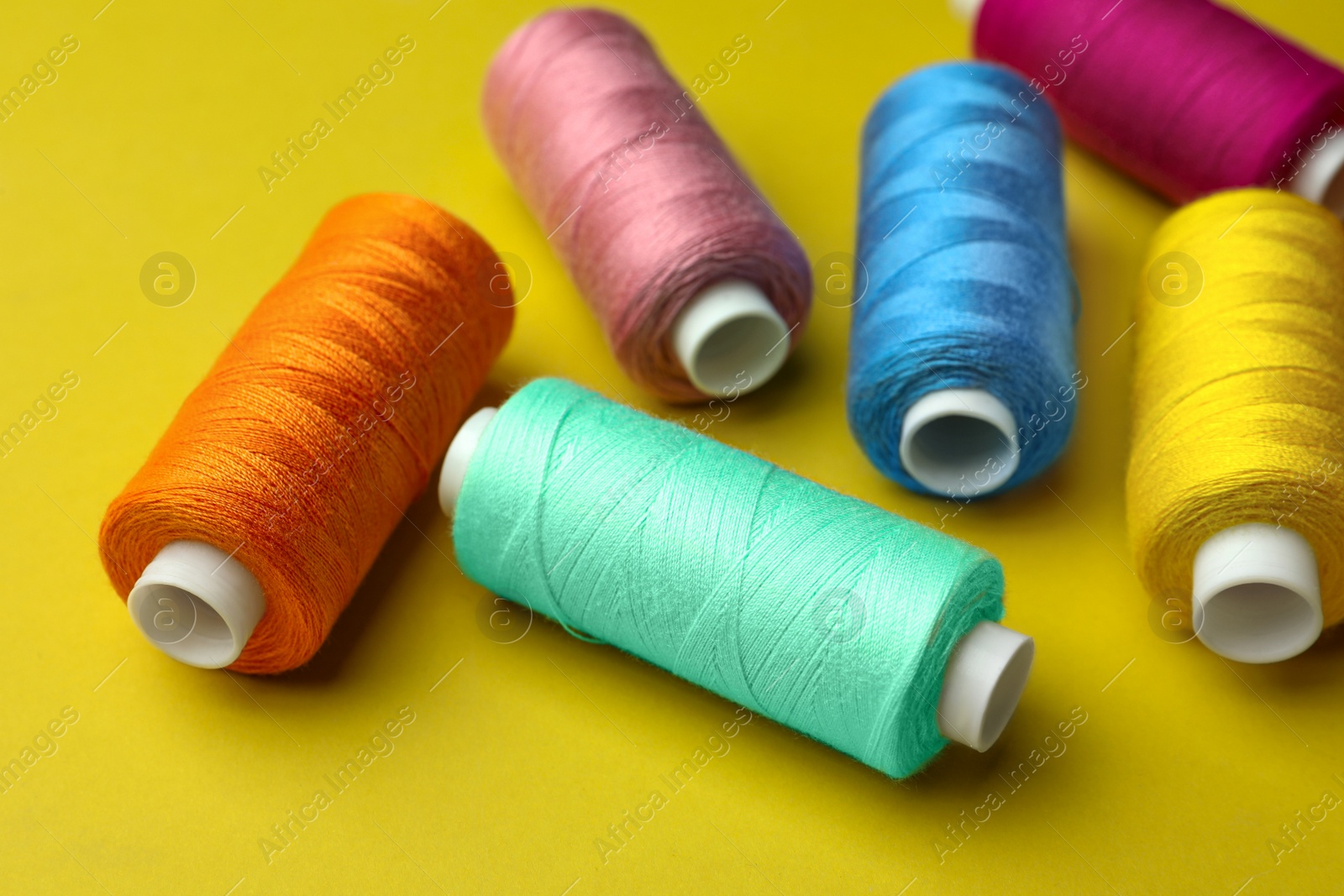 Photo of Different colorful sewing threads on yellow background