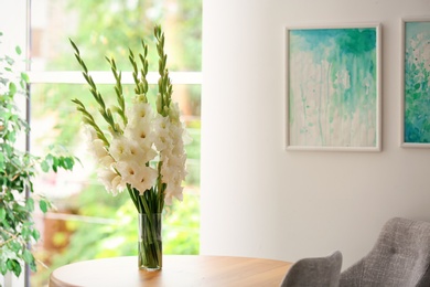 Photo of Vase with beautiful white gladiolus flowers on wooden table in room, space for text