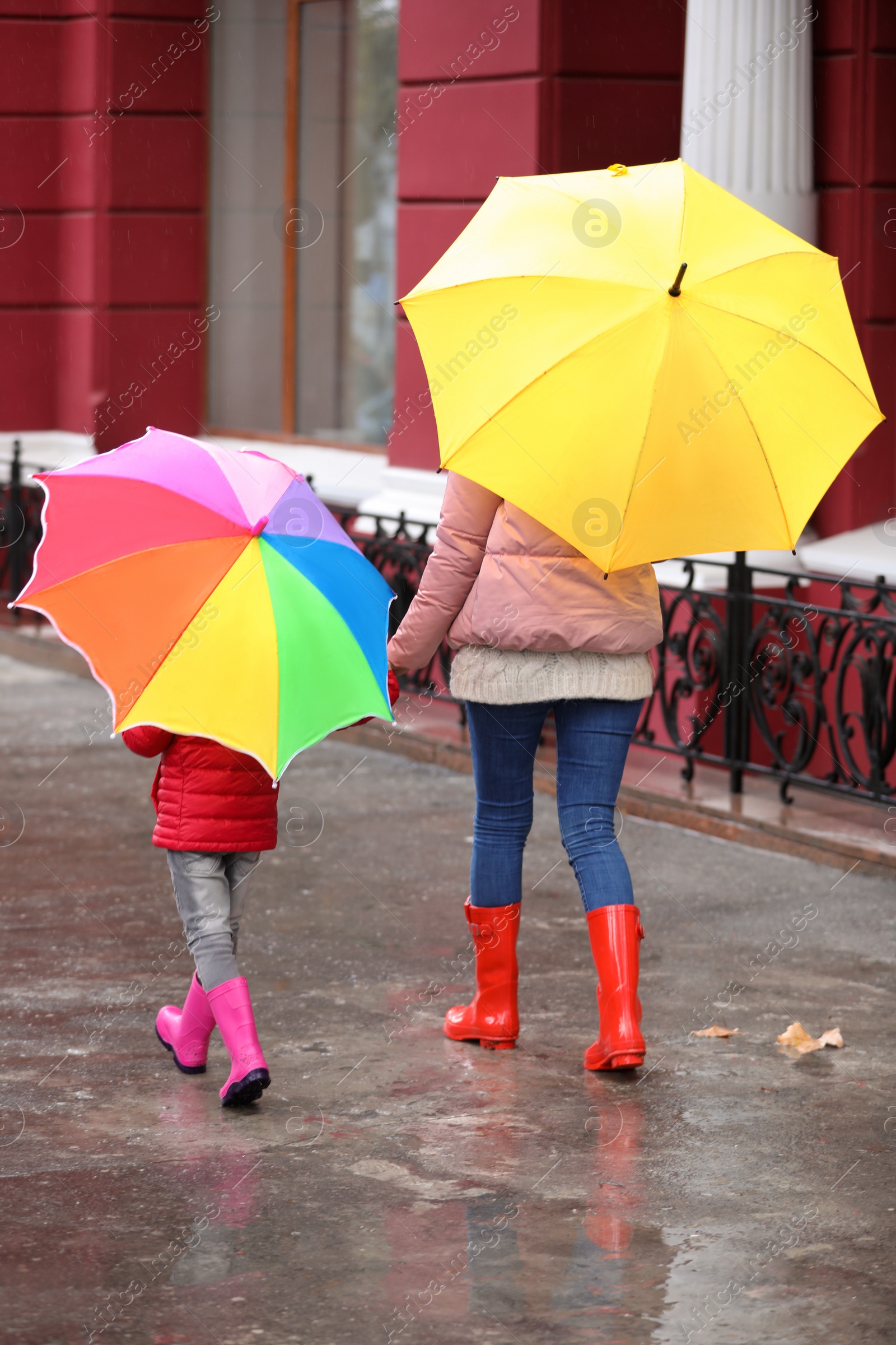 Photo of Mother and daughter with umbrellas taking autumn walk in city on rainy day