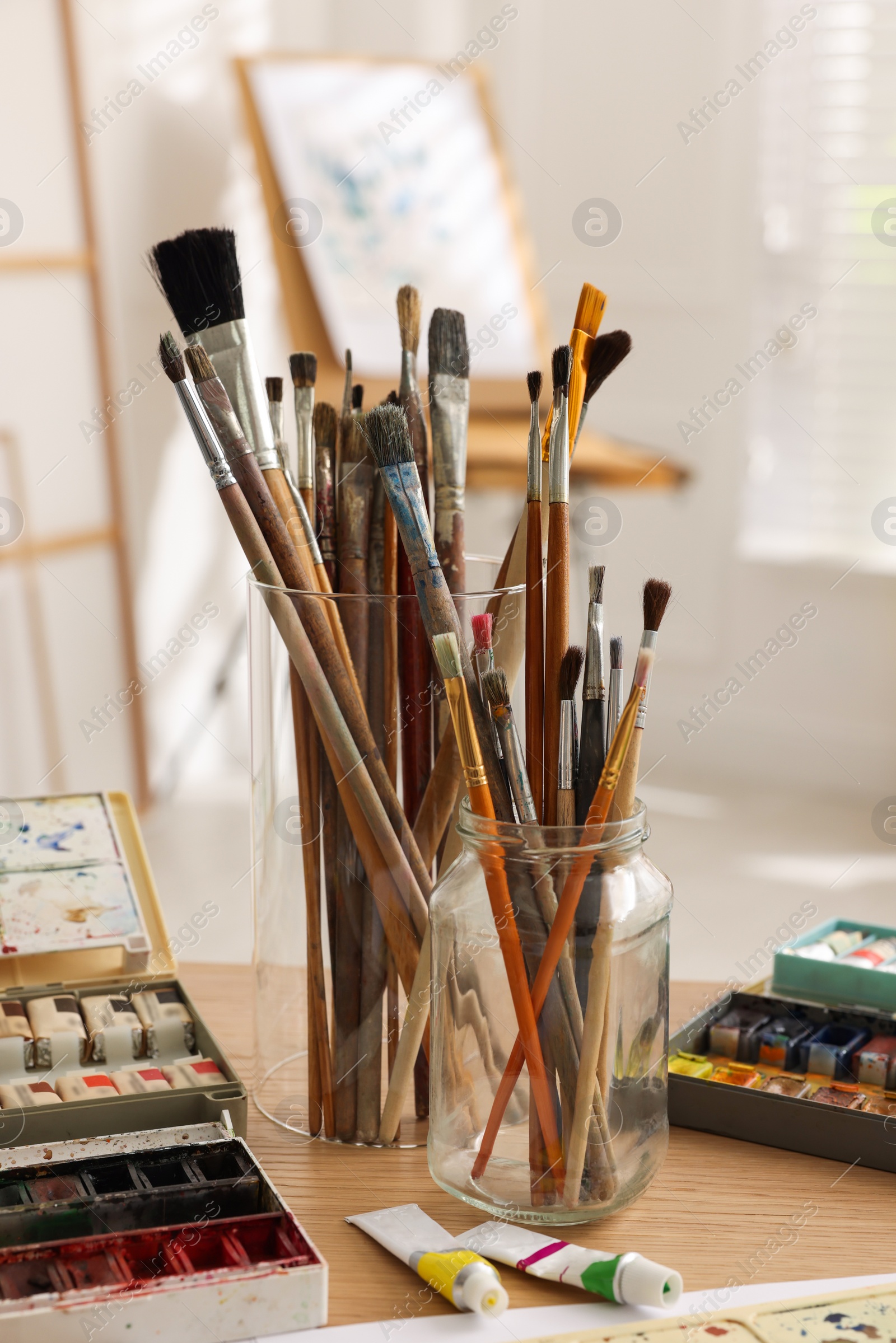 Photo of Different brushes and colorful paints on wooden table in studio. Artist's workplace