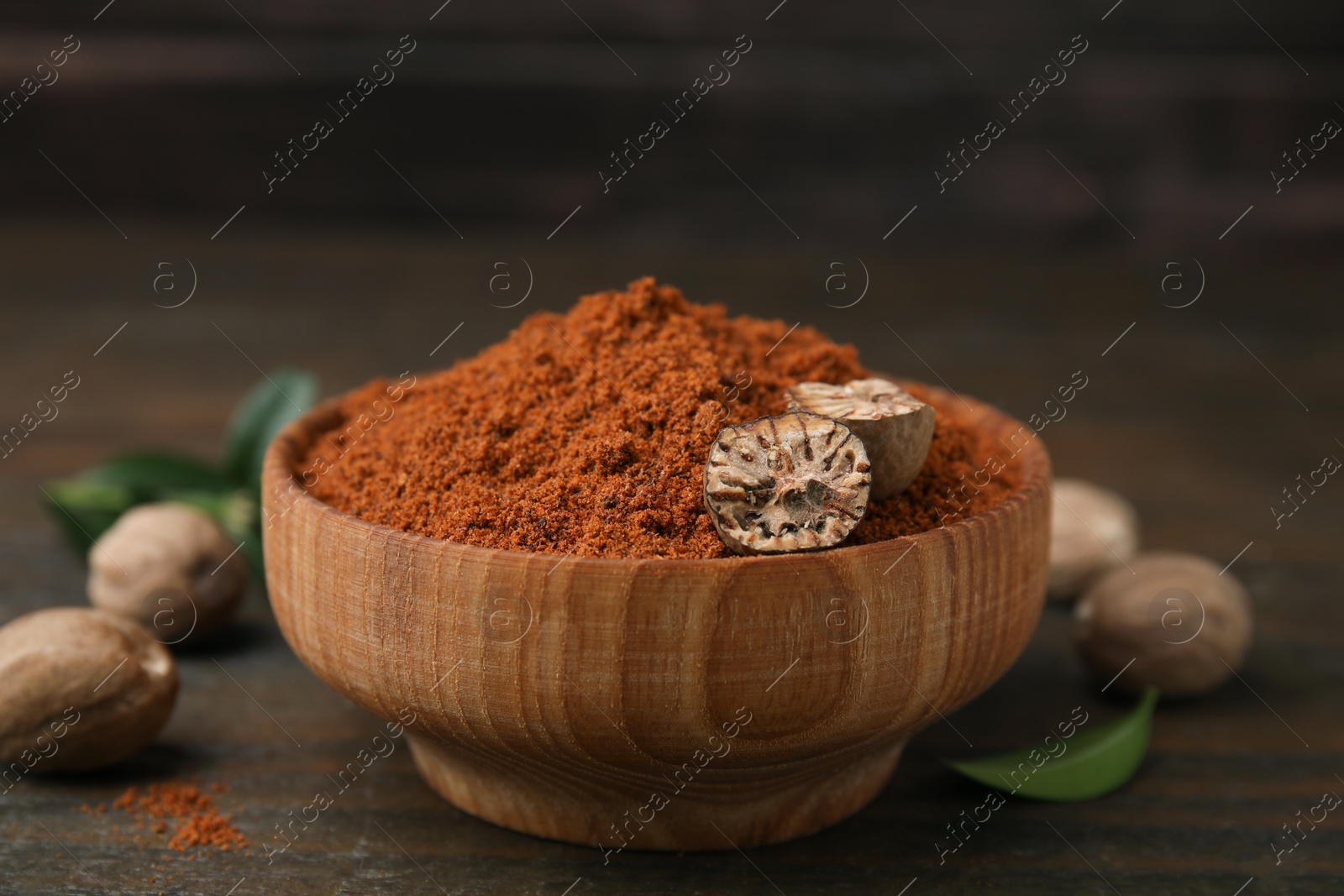 Photo of Nutmeg powder and halves of seed in bowl on wooden table, closeup