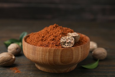 Photo of Nutmeg powder and halves of seed in bowl on wooden table, closeup
