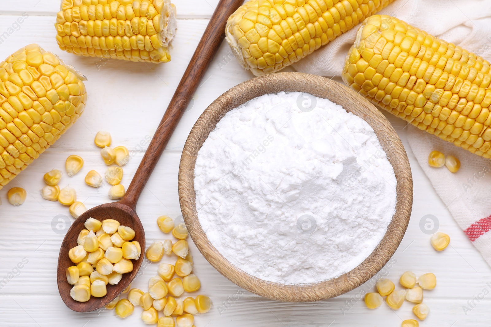 Photo of Bowl with corn starch, ripe cobs and kernels on white wooden table, flat lay