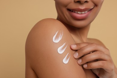 Photo of Young woman applying body cream onto shoulder on beige background, closeup