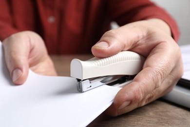 Man stapling papers at wooden table, closeup