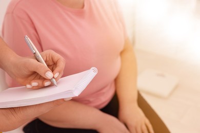 Nutritionist with notebook consulting overweight woman in clinic, closeup