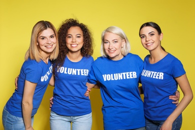 Team of female volunteers in uniform on yellow background