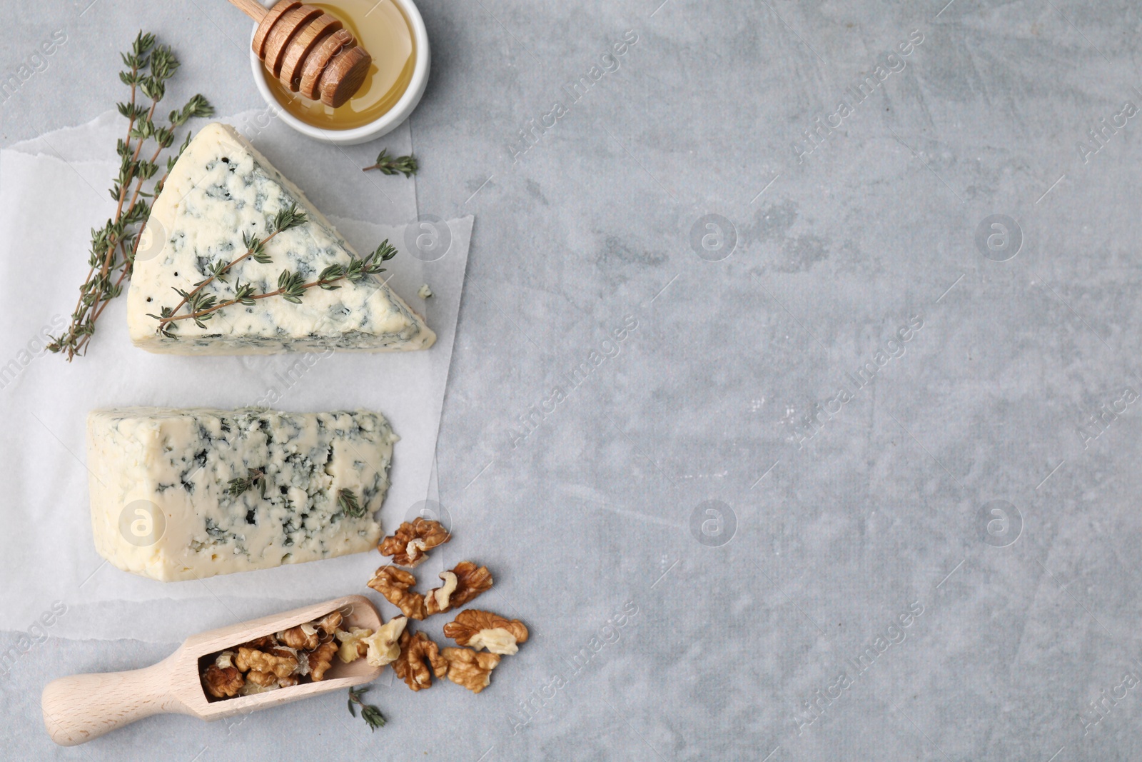 Photo of Tasty blue cheese with thyme, honey and walnuts on grey table, flat lay. Space for text