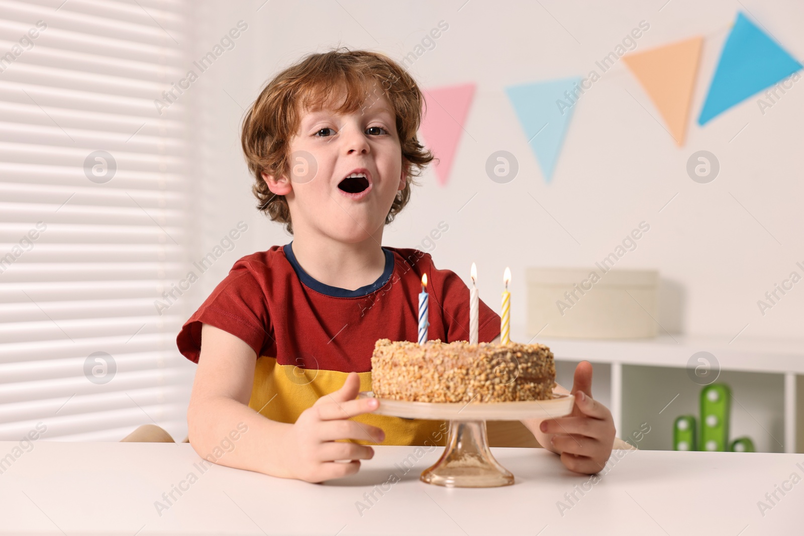 Photo of Cute boy with birthday cake at table indoors