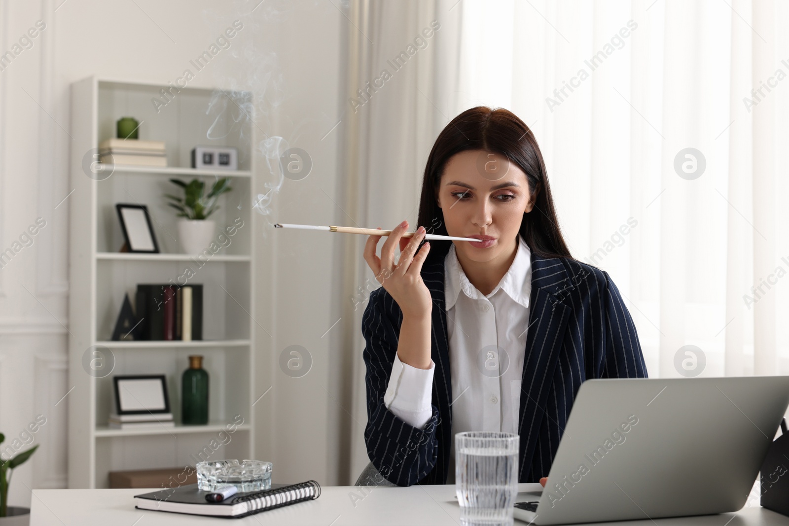 Photo of Woman using long cigarette holder for smoking at workplace in office