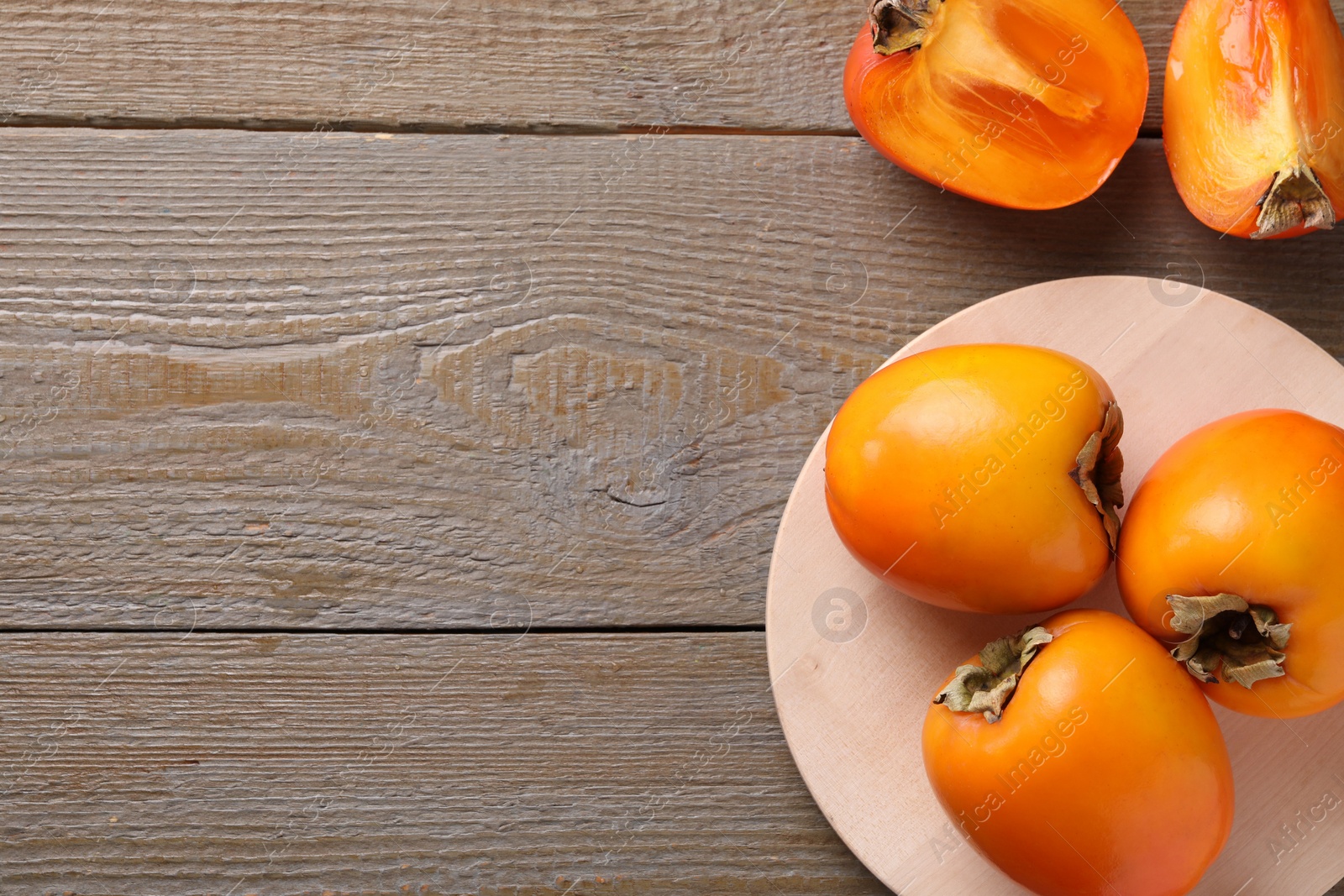 Photo of Whole and cut delicious ripe persimmons on wooden table, flat lay. Space for text