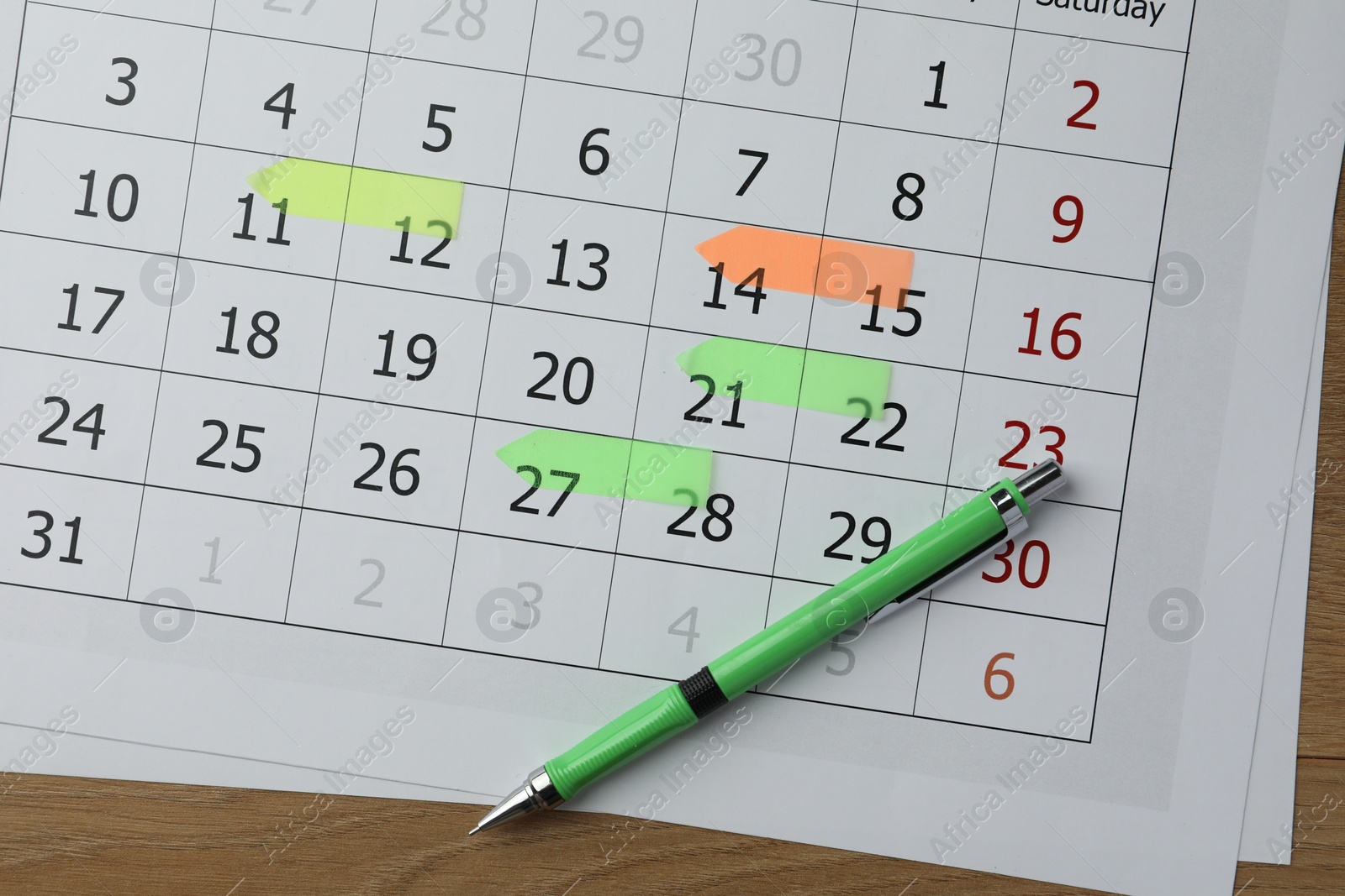 Photo of Timetable. Calendar page with marked dates and pen on wooden table, top view