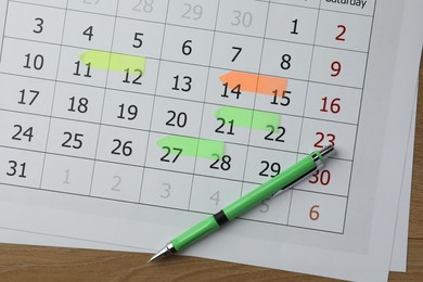 Timetable. Calendar page with marked dates and pen on wooden table, top view