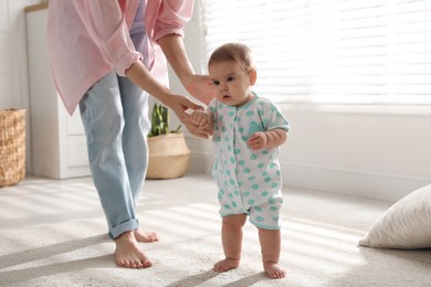 Photo of Mother supporting her baby daughter while she learning to walk at home