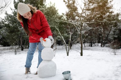 Photo of Young woman making snowman outdoors on winter day. Space for text