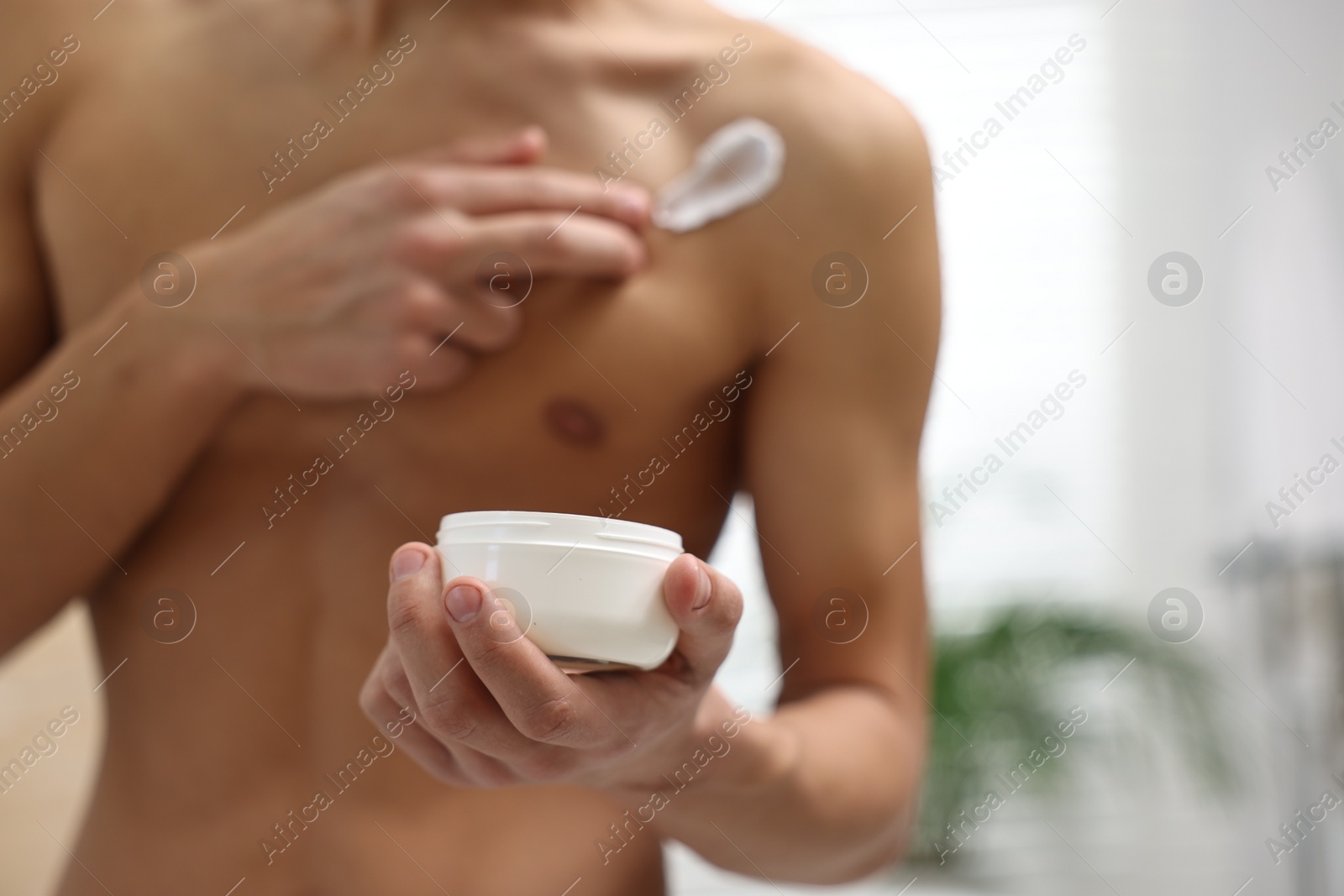 Photo of Man applying moisturizing cream onto his shoulder in bathroom, closeup. Space for text