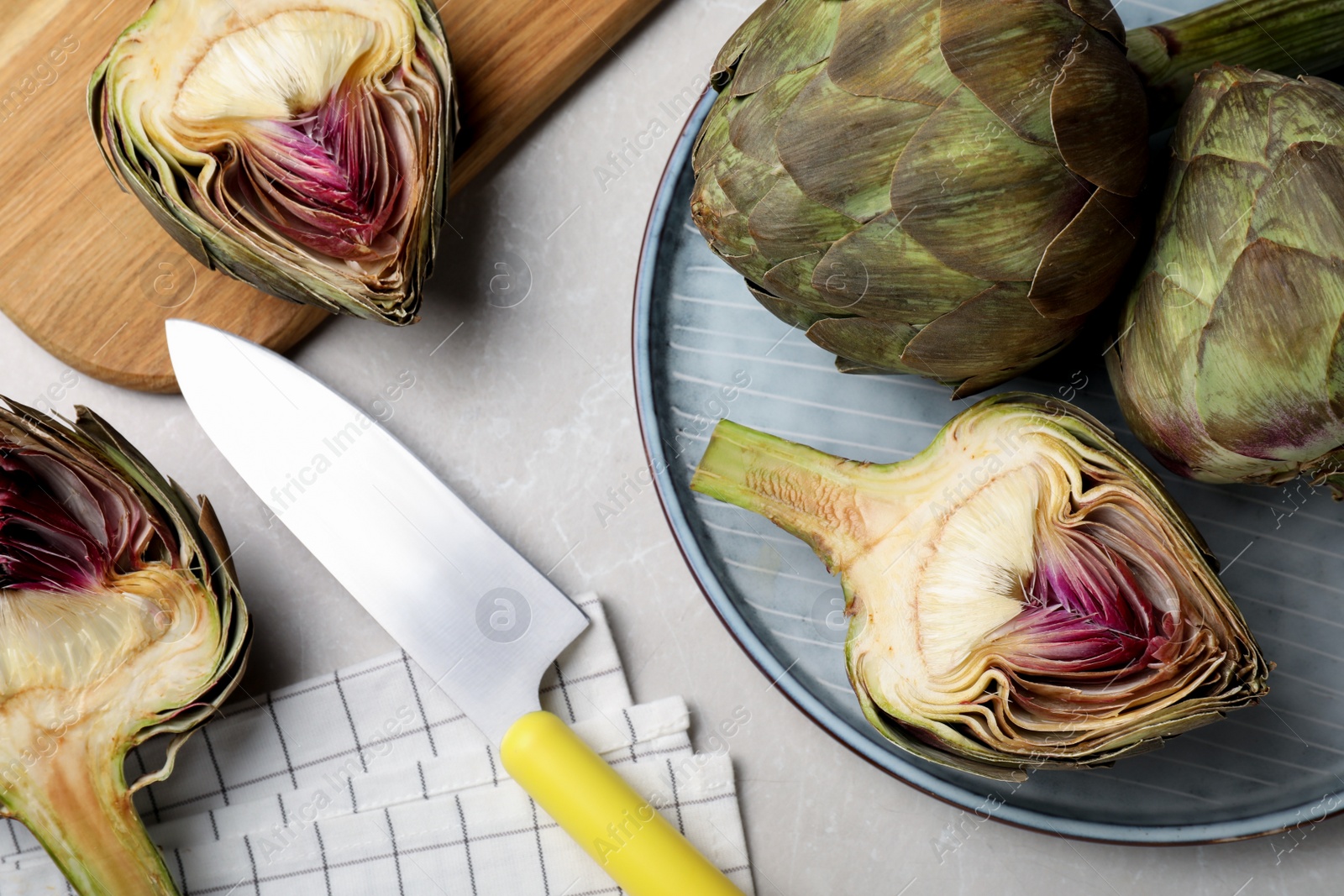 Photo of Cut and whole fresh raw artichokes on light table, flat lay