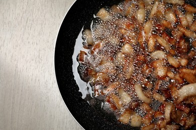 Tasty cooked cracklings in frying pan on light wooden table, top view. Pork lard