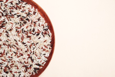 Mixed brown and other types of rice in wooden plate on light background. Top view with space for text