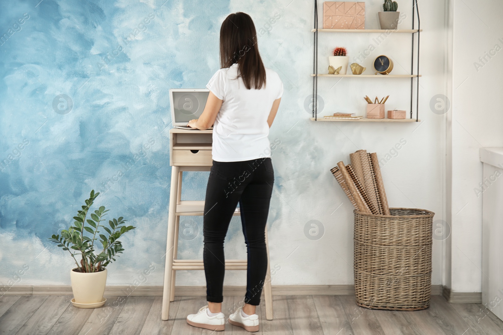 Photo of Young woman using laptop at stand up workplace in room