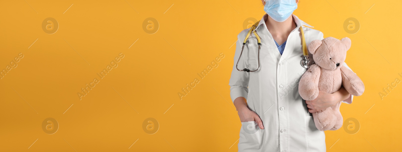 Photo of Pediatrician with teddy bear and stethoscope on yellow background, closeup