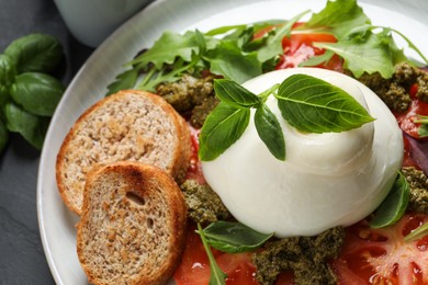 Photo of Delicious burrata salad with tomatoes, arugula and pesto sauce on table, closeup