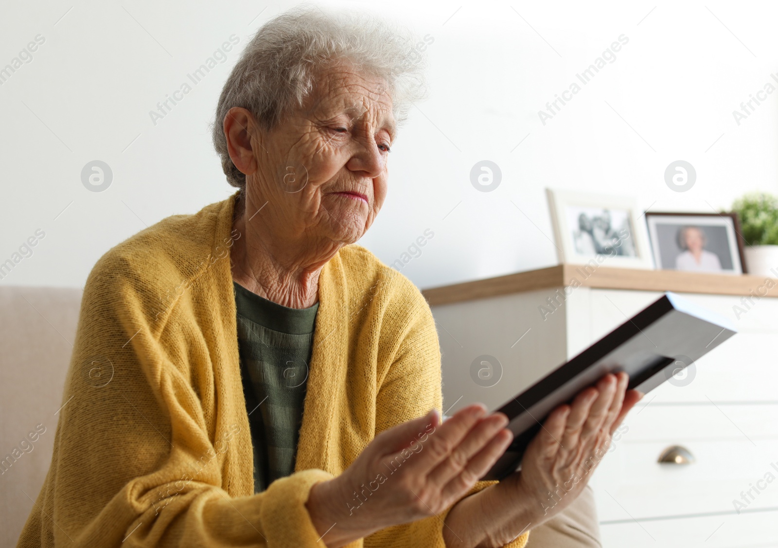 Photo of Elderly woman with framed photo on sofa at home