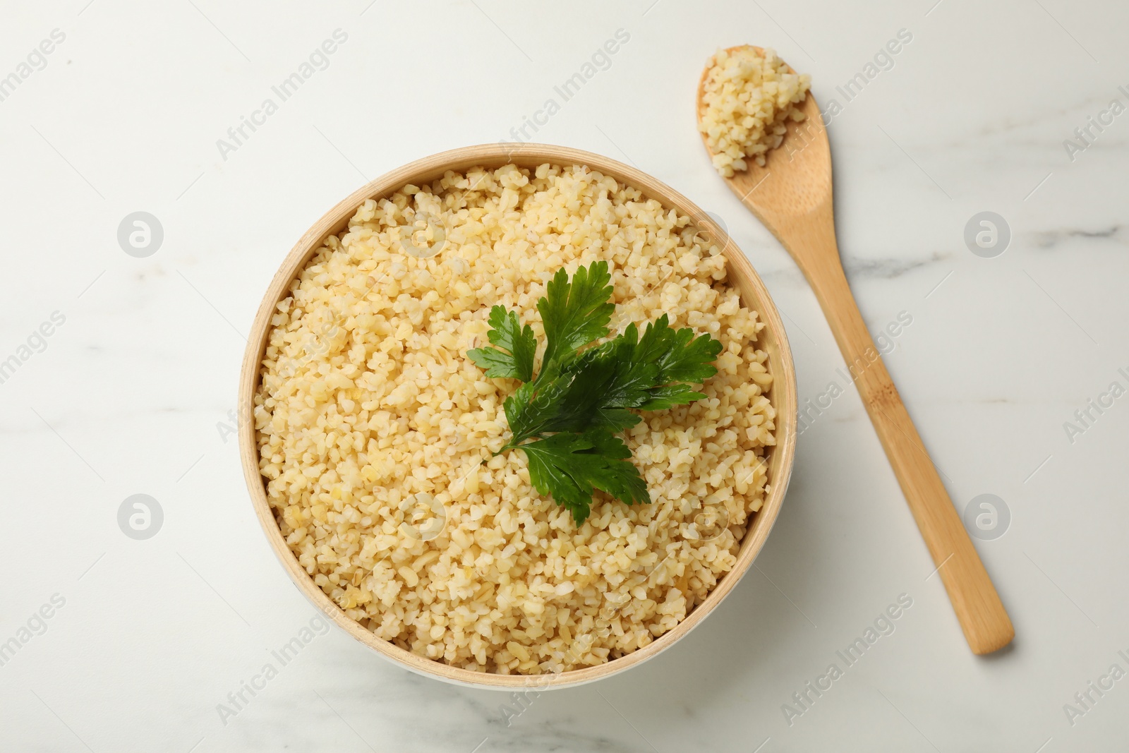 Photo of Delicious bulgur with parsley and spoon on white marble table, top view