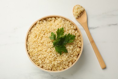 Photo of Delicious bulgur with parsley and spoon on white marble table, top view