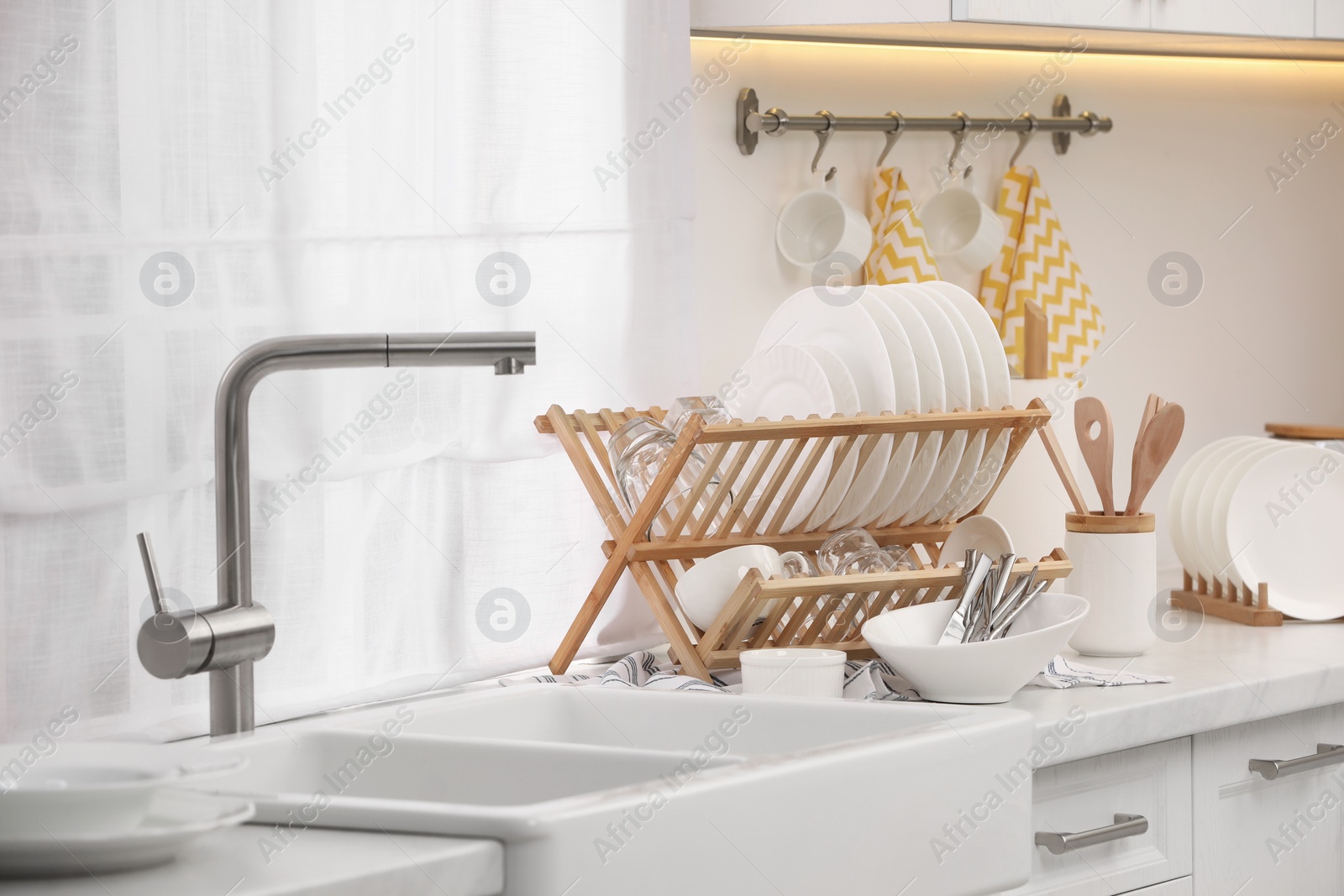 Photo of Sink and drying rack with clean dishes and cutlery on countertop in kitchen