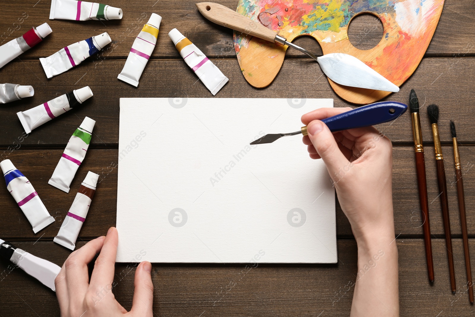 Photo of Man with spatula and blank canvas at wooden table, top view