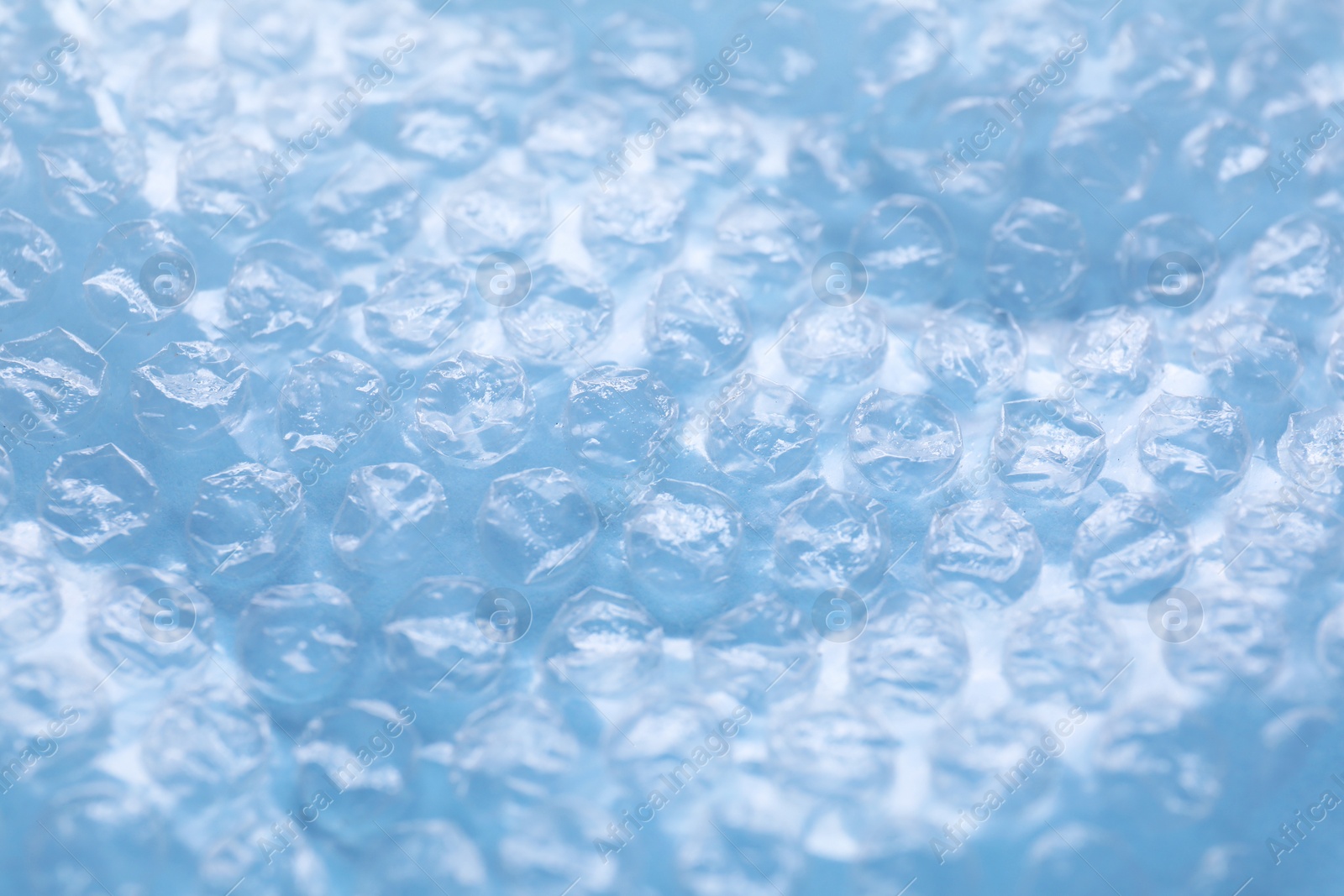 Photo of Transparent bubble wrap on light blue background, closeup